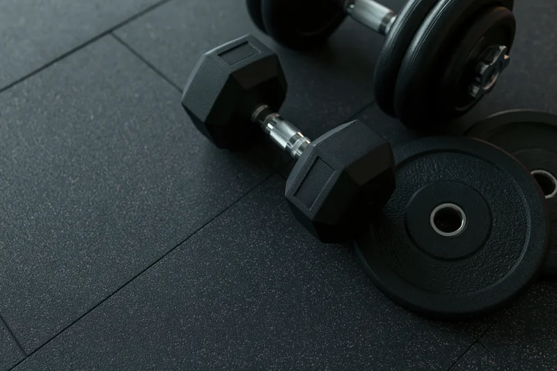 Black hexagonal dumbbell and weight plates resting on dark rubber gym floor