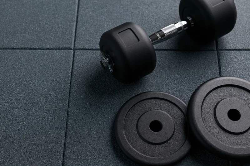Black metal dumbbell with two weight plates resting on dark textured gym floor