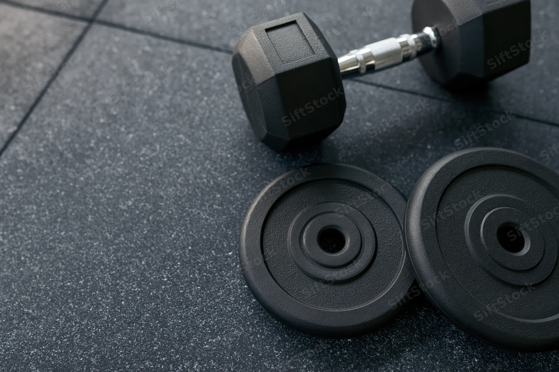 Black hex dumbbell and two weight plates resting on dark rubber gym floor