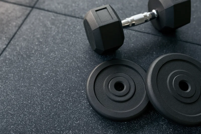 Black hex dumbbell and two weight plates resting on dark rubber gym floor