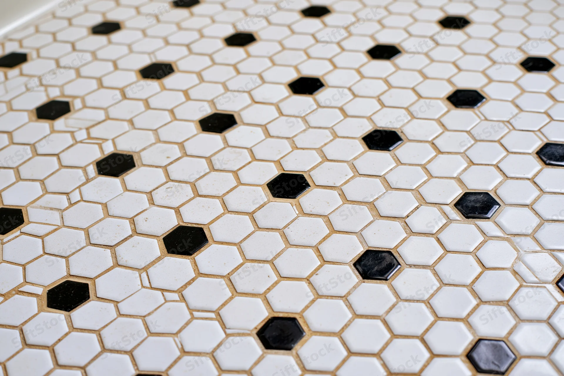 Hexagonal mosaic tile floor with white and black tiles arranged in a repeating pattern, grouted in beige, viewed flat-on