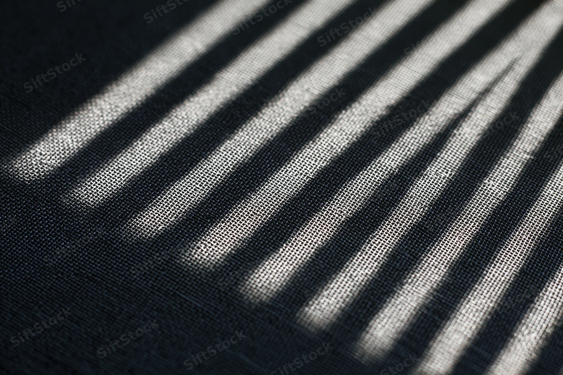 Close-up of dark grey window screen mesh with diagonal light and shadow stripes across its textured surface
