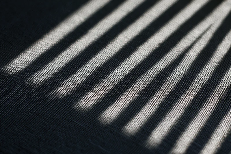 Close-up of dark grey window screen mesh with diagonal light and shadow stripes across its textured surface