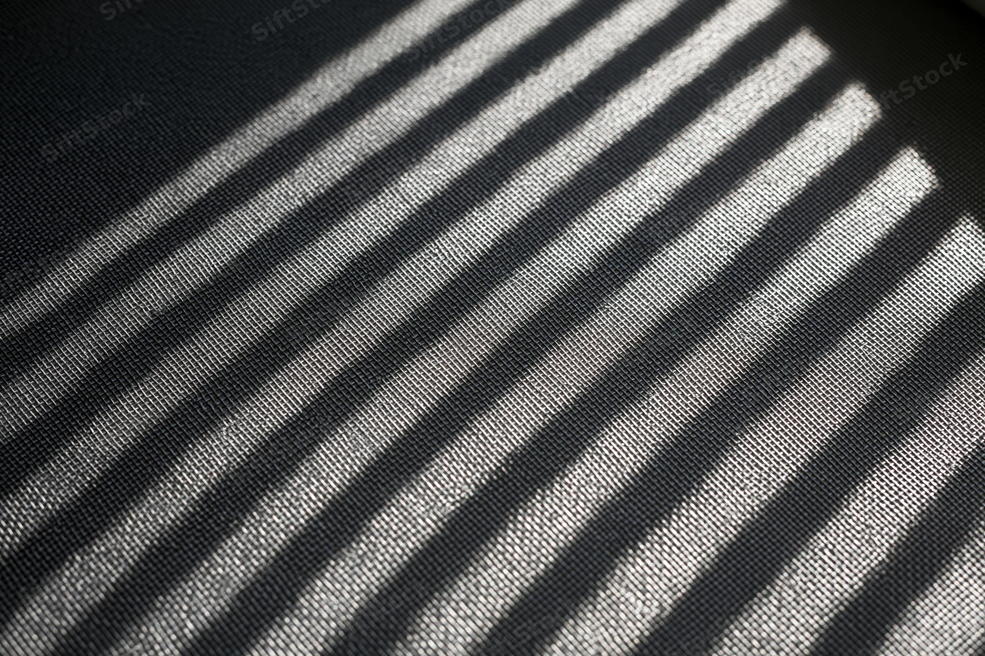 Close-up of dark grey window screen mesh with diagonal light and shadow stripes in flat lay arrangement