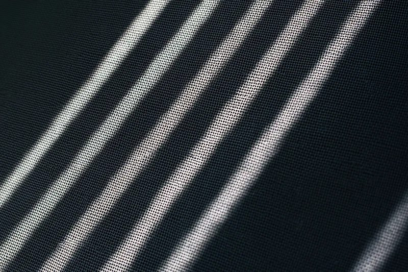 Close-up of dark grey window screen mesh with diagonal light patterns filling the frame