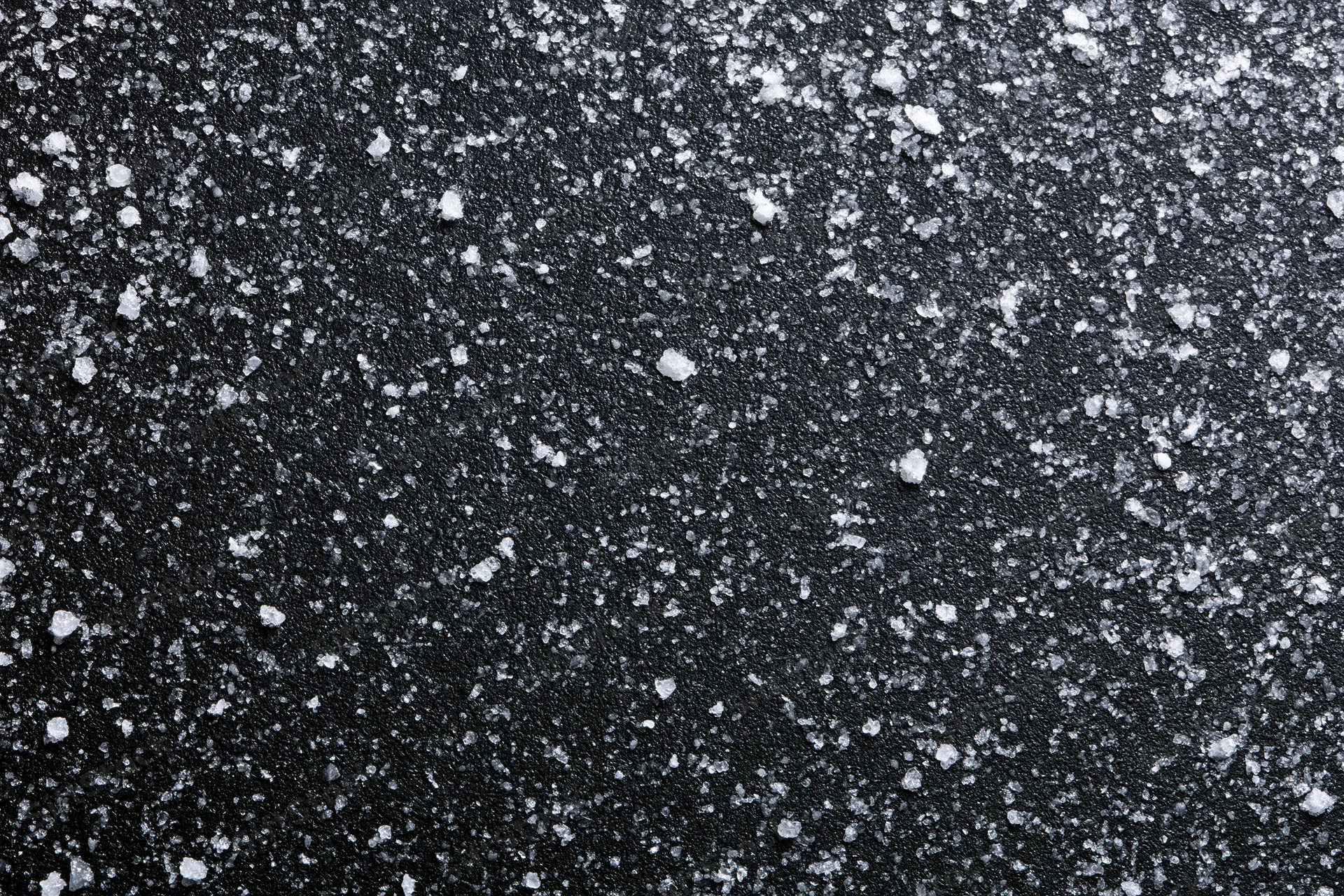 Close-up flat lay of a dark matte black surface covered in scattered white salt crystals