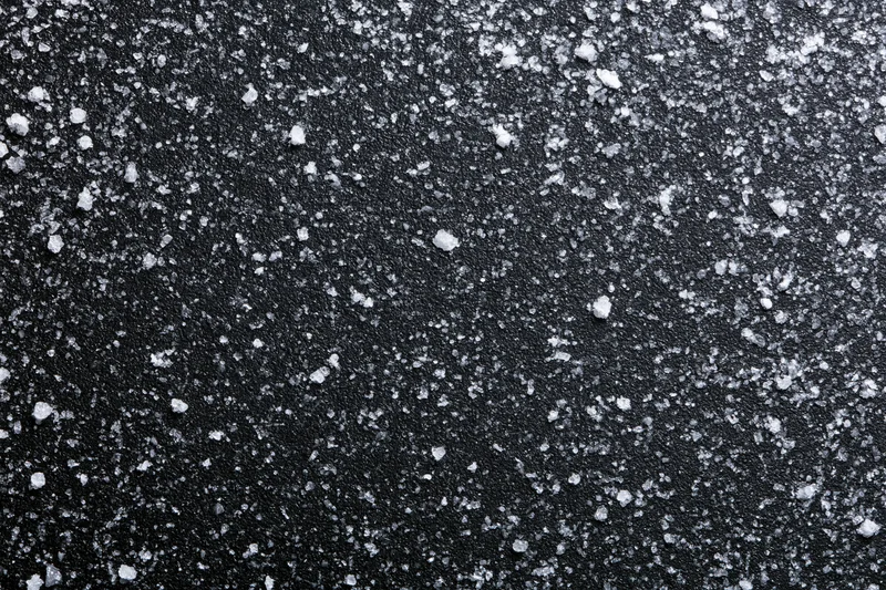 Close-up flat lay of a dark matte black surface covered in scattered white salt crystals