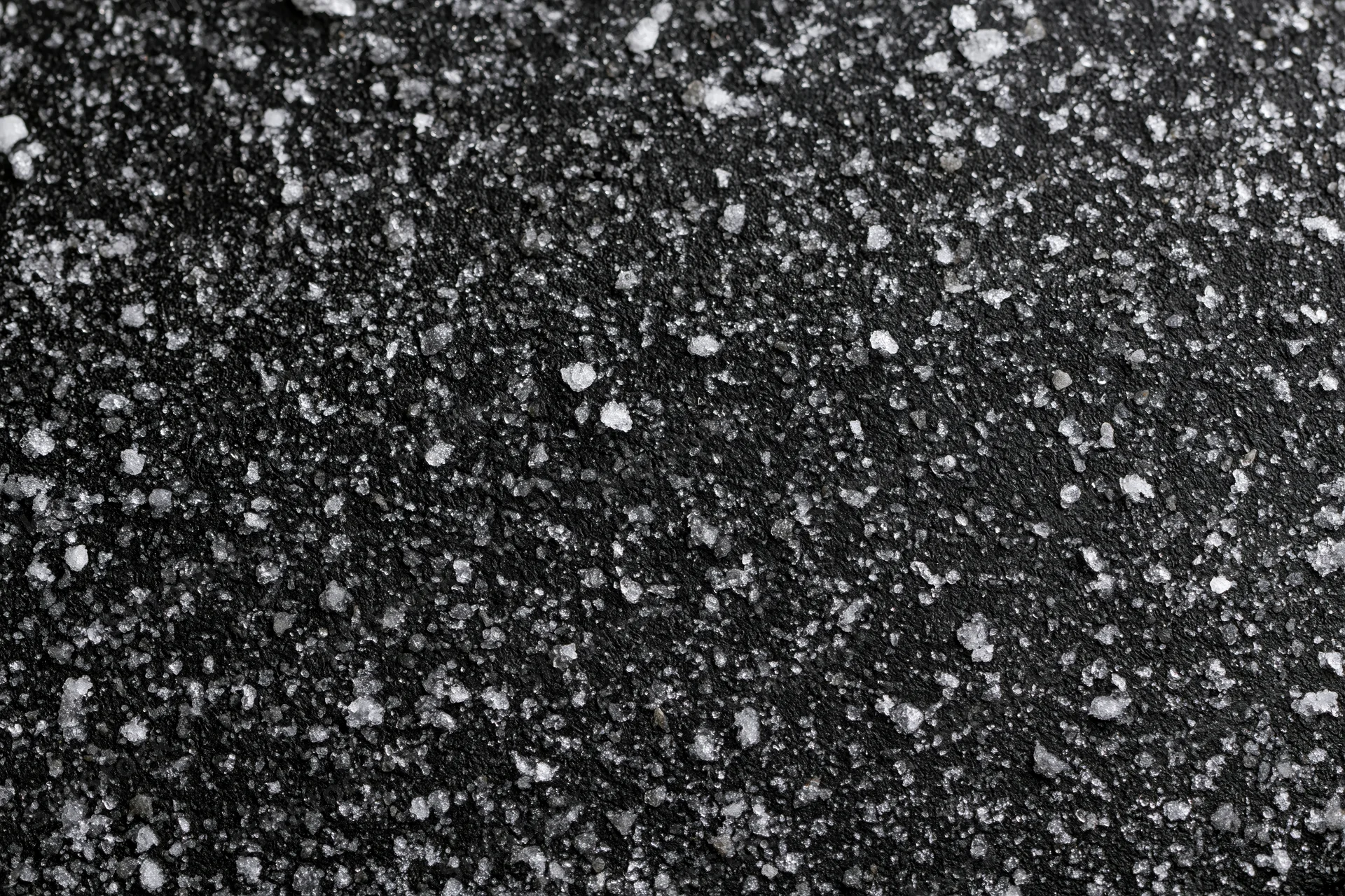 Dark matte black surface covered in scattered white crystalline particles in flat lay closeup