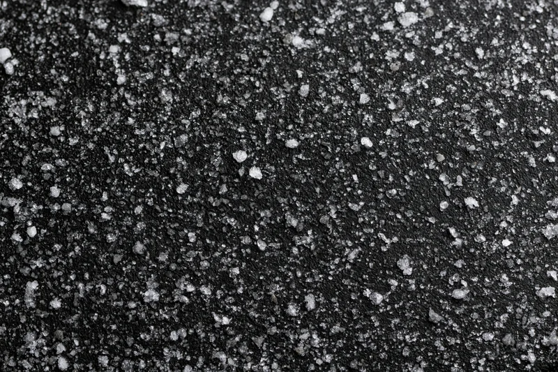 Dark matte black surface covered in scattered white crystalline particles in flat lay closeup