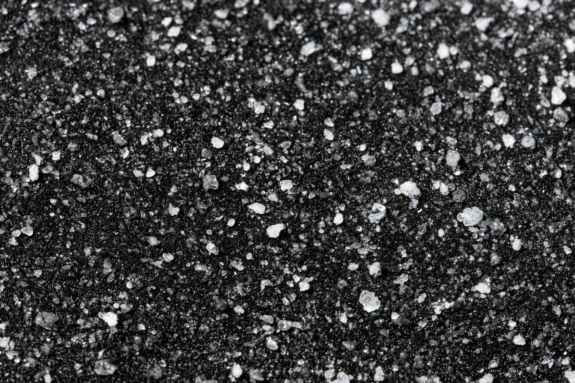 Close-up of a dark matte black surface covered in scattered white granular particles arranged in a flat lay