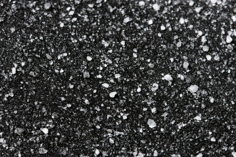 Close-up of a dark matte black surface covered in scattered white granular particles arranged in a flat lay