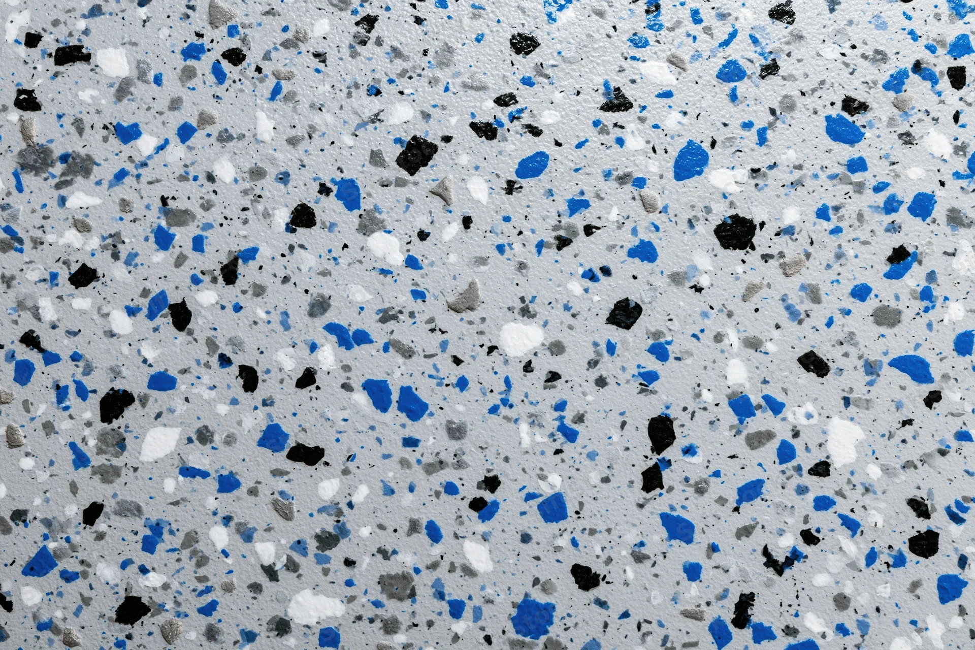 Close-up of epoxy garage floor coating with blue black and white speckles scattered across gray surface