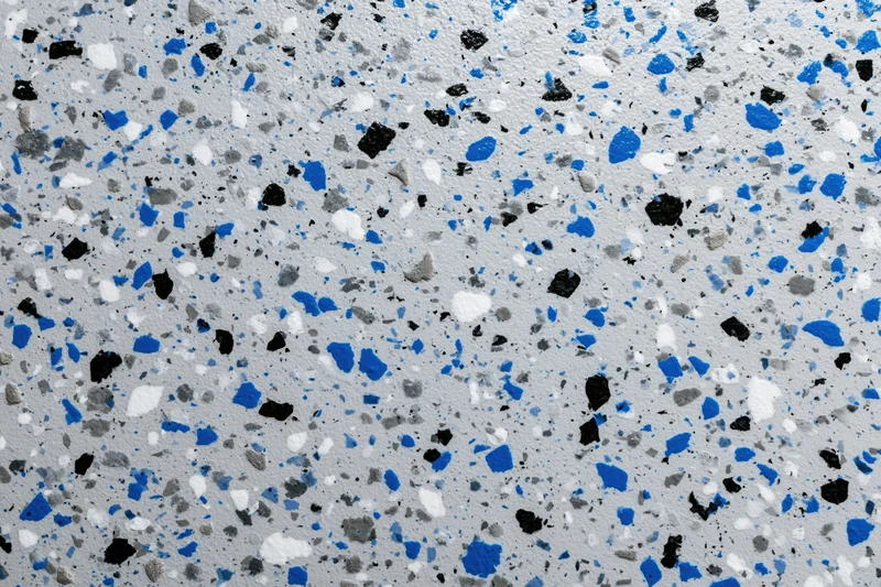 Close-up of epoxy garage floor coating with blue black and white speckles scattered across gray surface