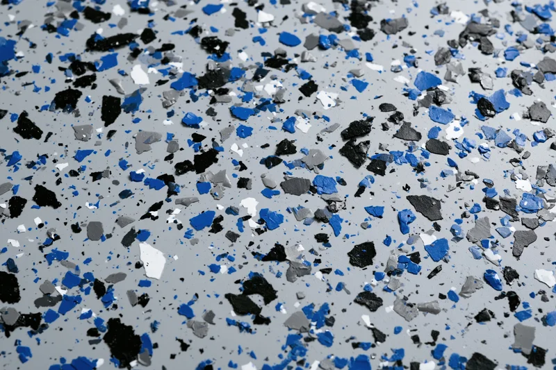 Close-up of speckled epoxy garage floor coating with blue black white and gray aggregate embedded in gray resin surface