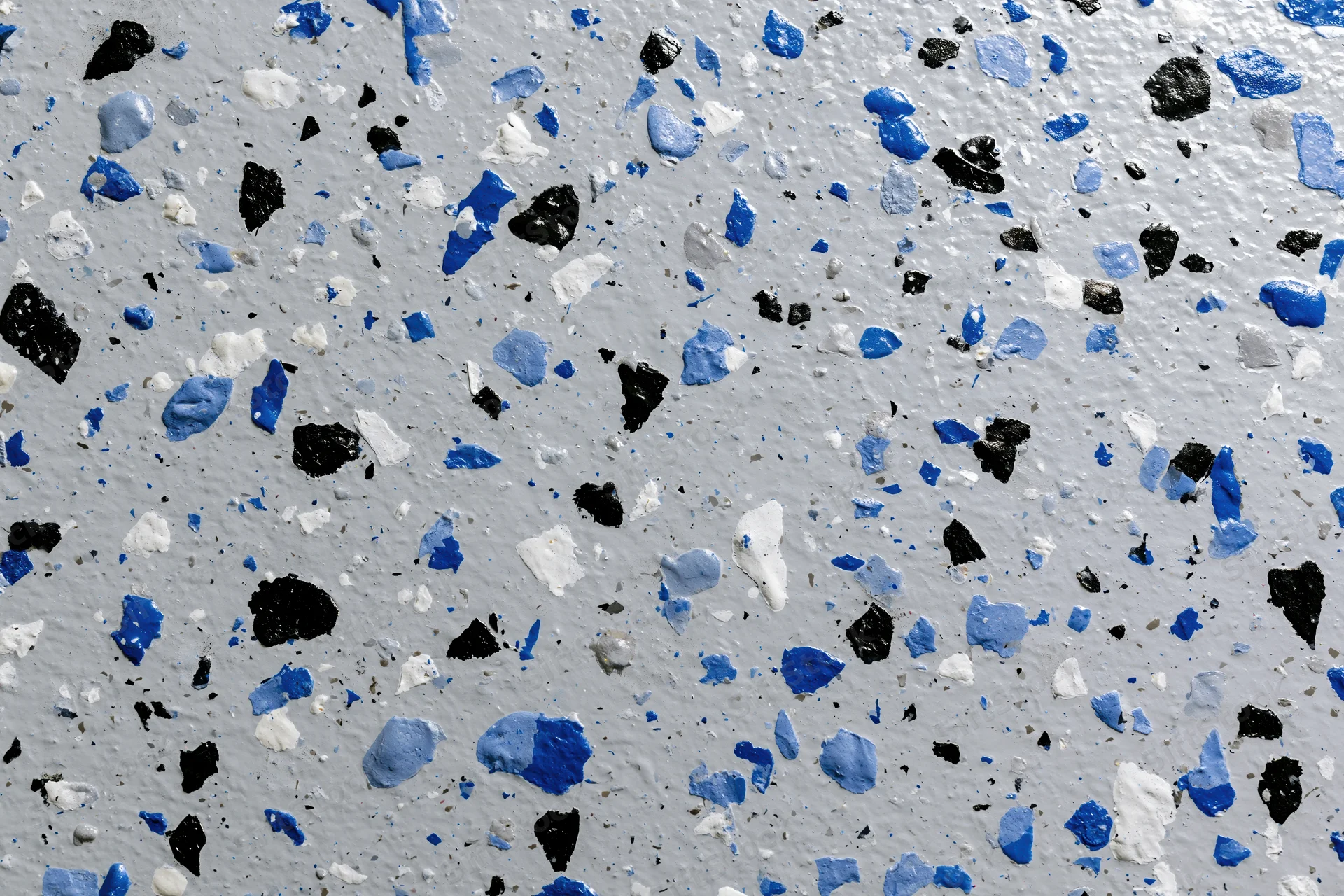 Close-up of epoxy garage floor coating with blue black and white speckles scattered across gray surface