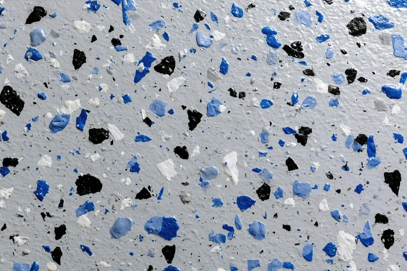 Close-up of epoxy garage floor coating with blue black and white speckles scattered across gray surface