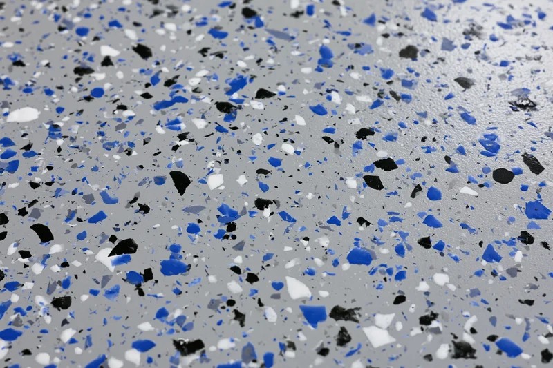 Close-up of speckled epoxy garage floor coating with blue black and white aggregate embedded in gray resin surface