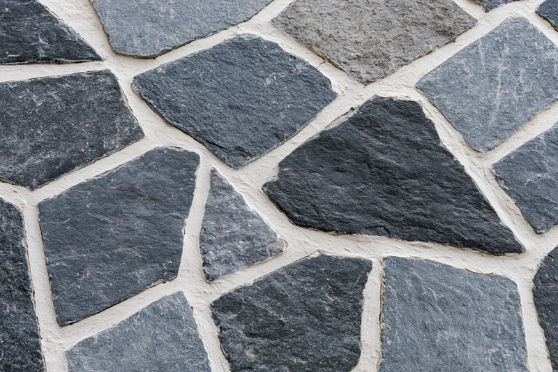 Irregular gray and black cobblestones set in white mortar forming a textured pavement surface