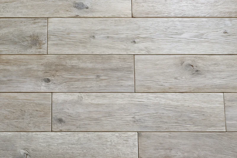 Close-up flat lay of light grey-beige hardwood floor planks arranged in staggered pattern showing natural wood grain and knots