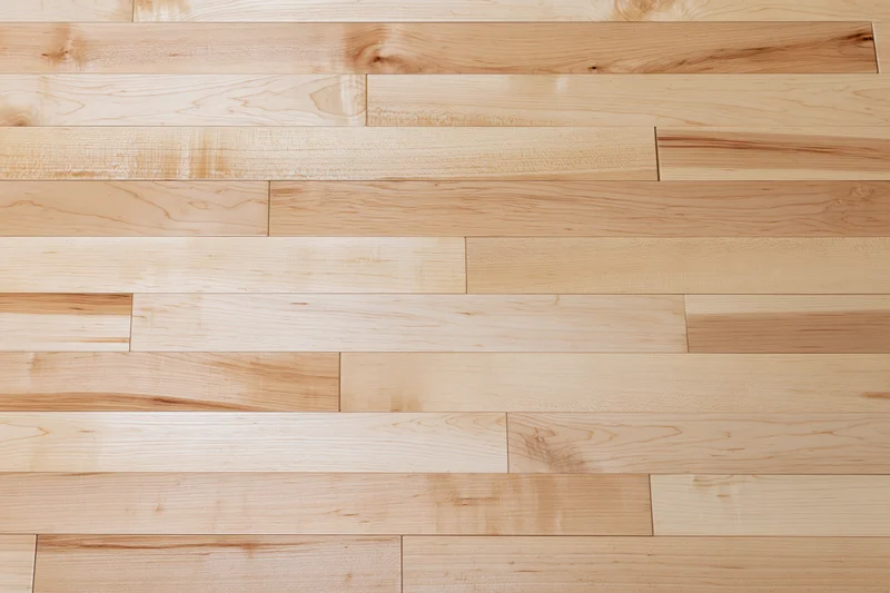 Close-up flat lay of light maple hardwood floor planks arranged in staggered rows showing natural wood grain and texture