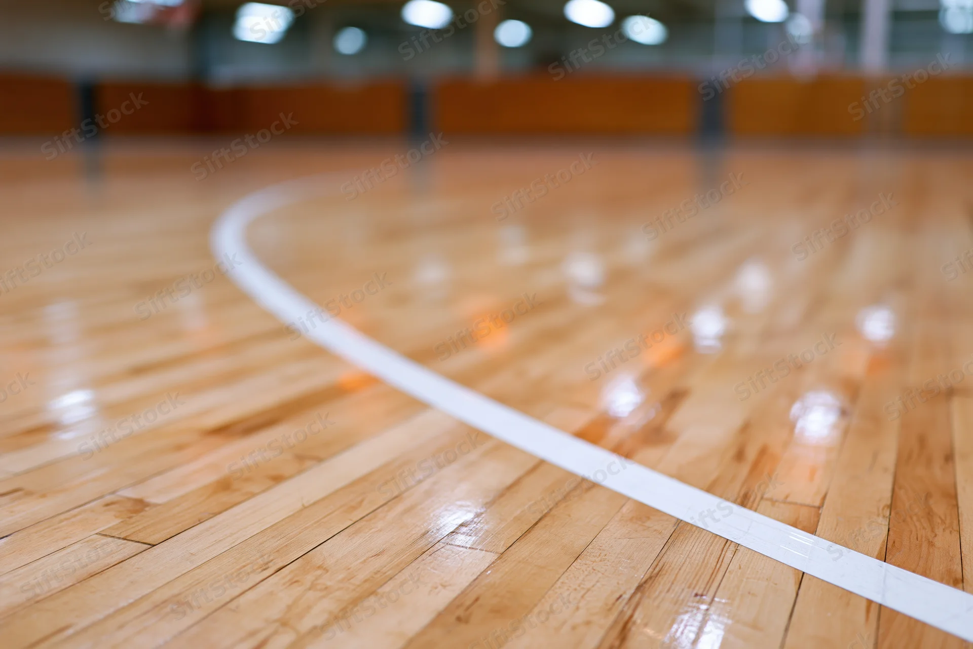 Polished hardwood gymnasium floor with white curved line and reflections under indoor lighting