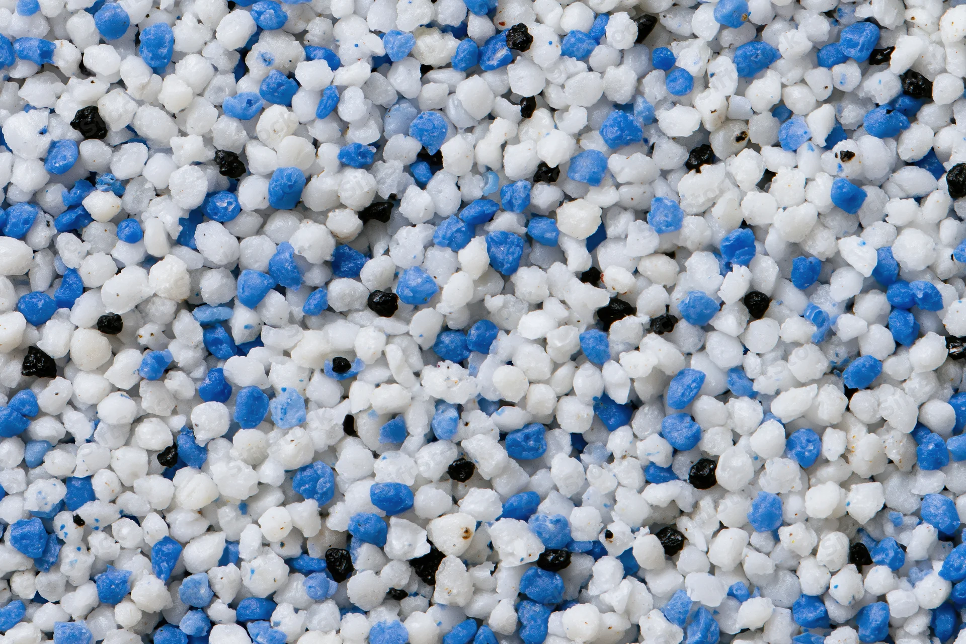 Close-up of mixed white blue and black plastic polymer granules scattered densely across frame