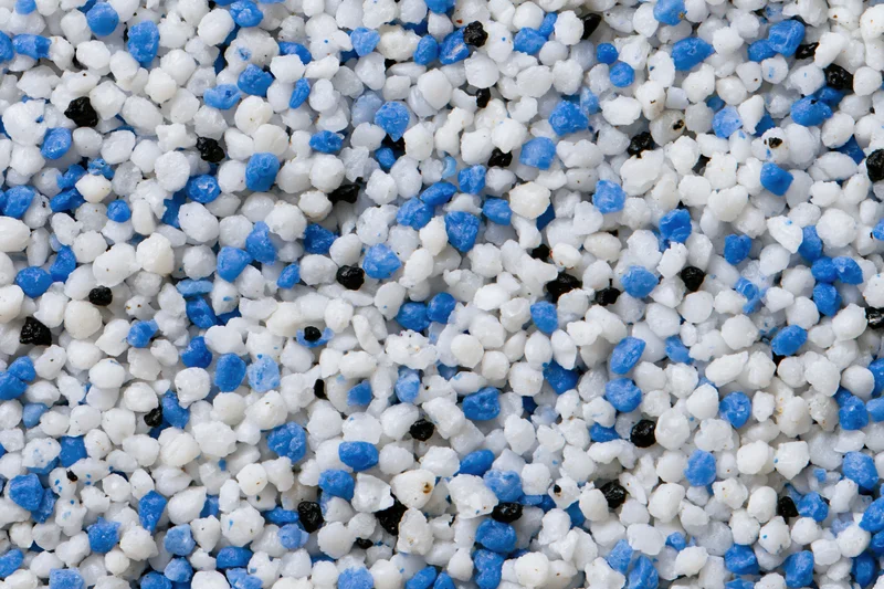 Close-up of mixed white blue and black plastic polymer granules scattered densely across frame