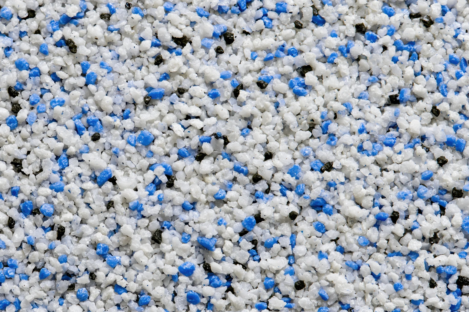 Mixed plastic polymer granules in white blue and black scattered across frame
