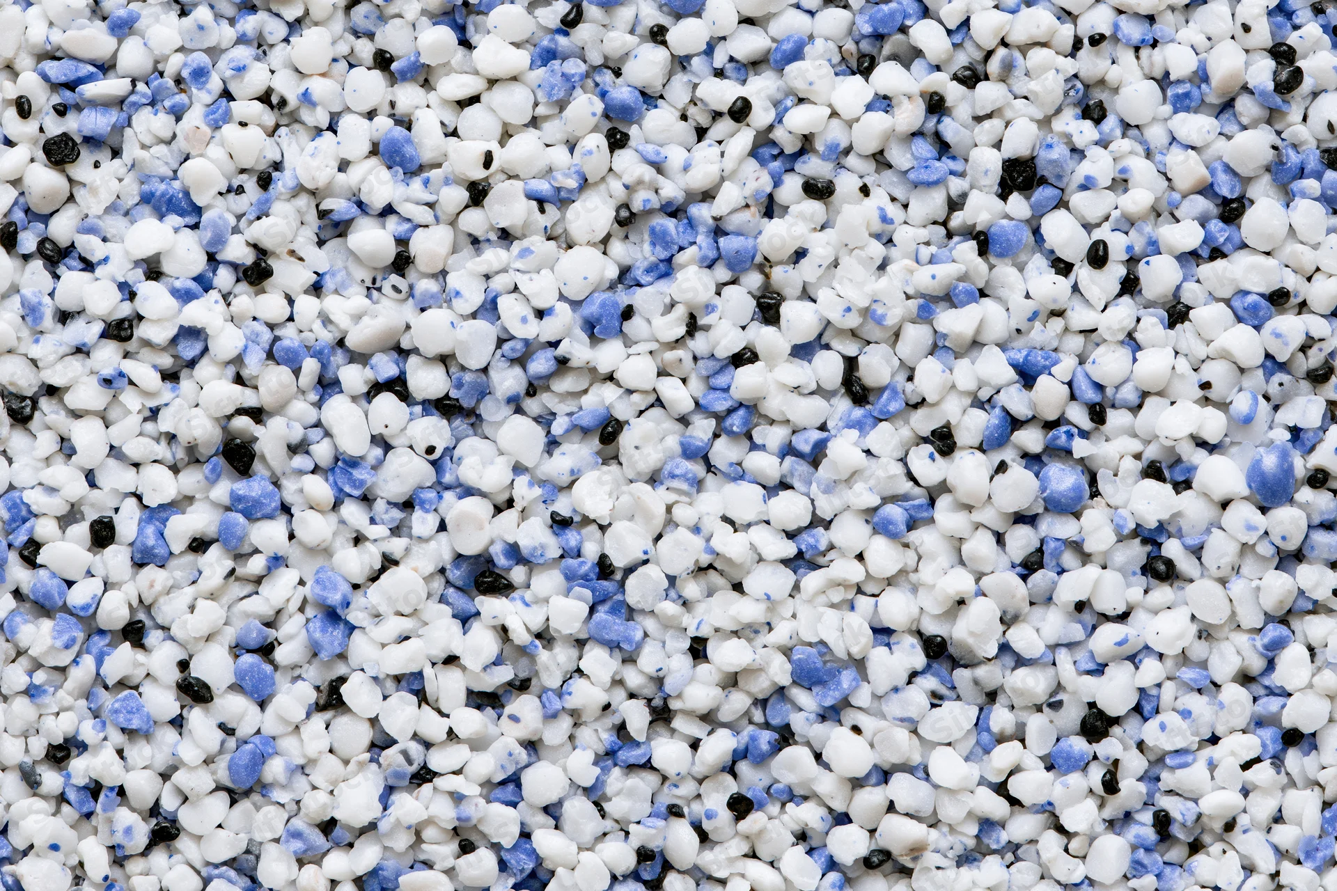 Mixed plastic polymer granules in white blue and black scattered across frame