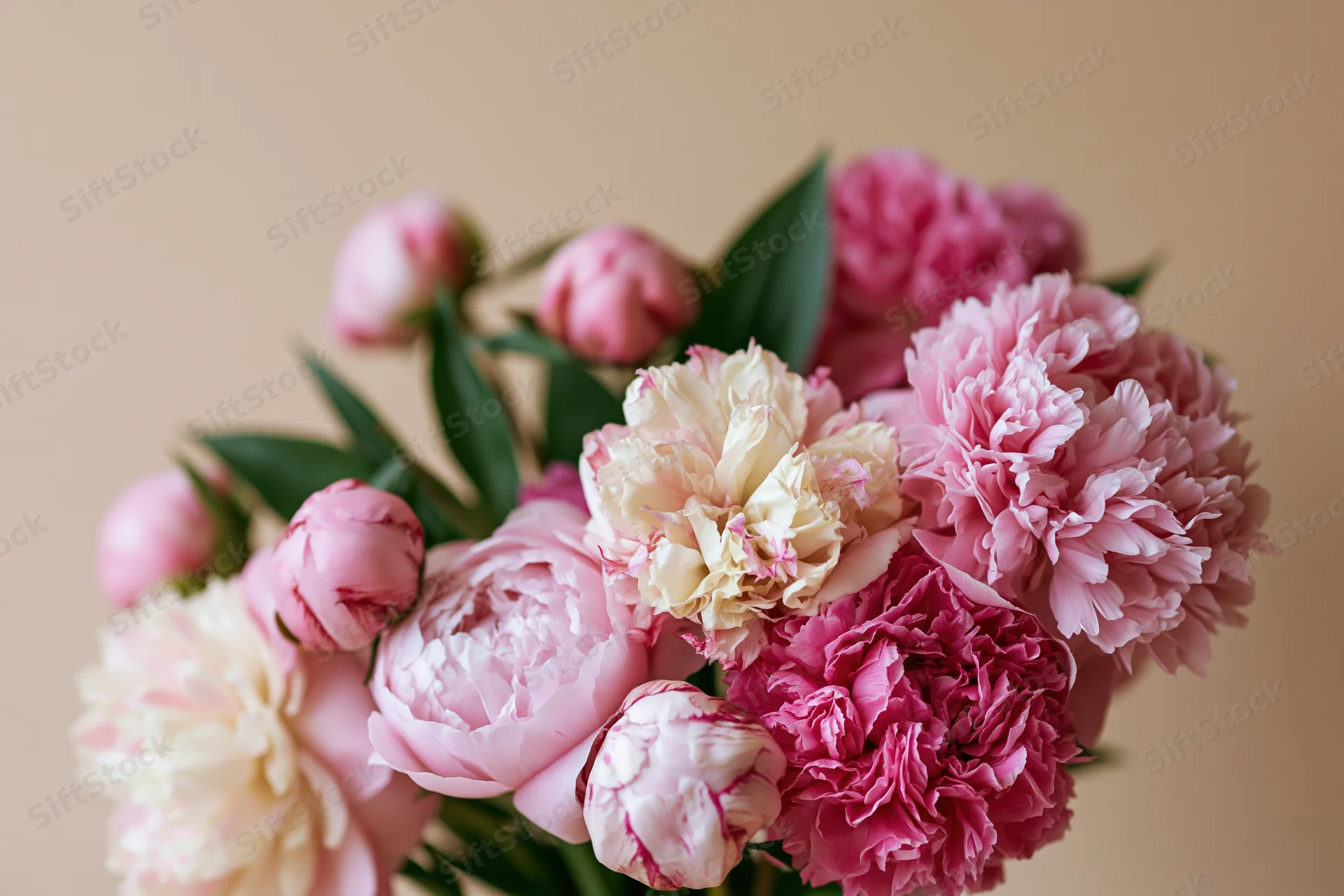 Close-up of a mixed bouquet of pink peonies in various stages of bloom with green stems and leaves against a neutral background