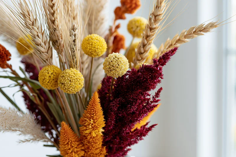 Close-up of a mixed dried flower arrangement with wheat, amaranthus, and billy balls in a rustic autumnal style