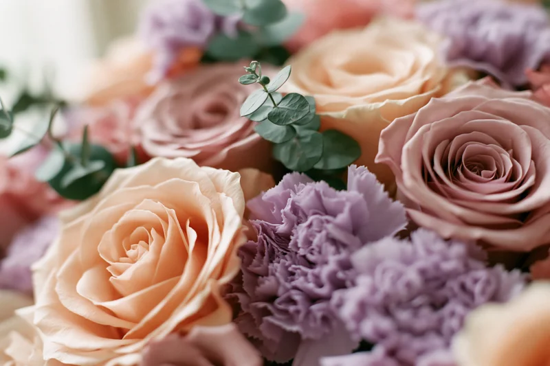 Close-up of a mixed floral bouquet with peach roses and lavender carnations arranged with eucalyptus greenery
