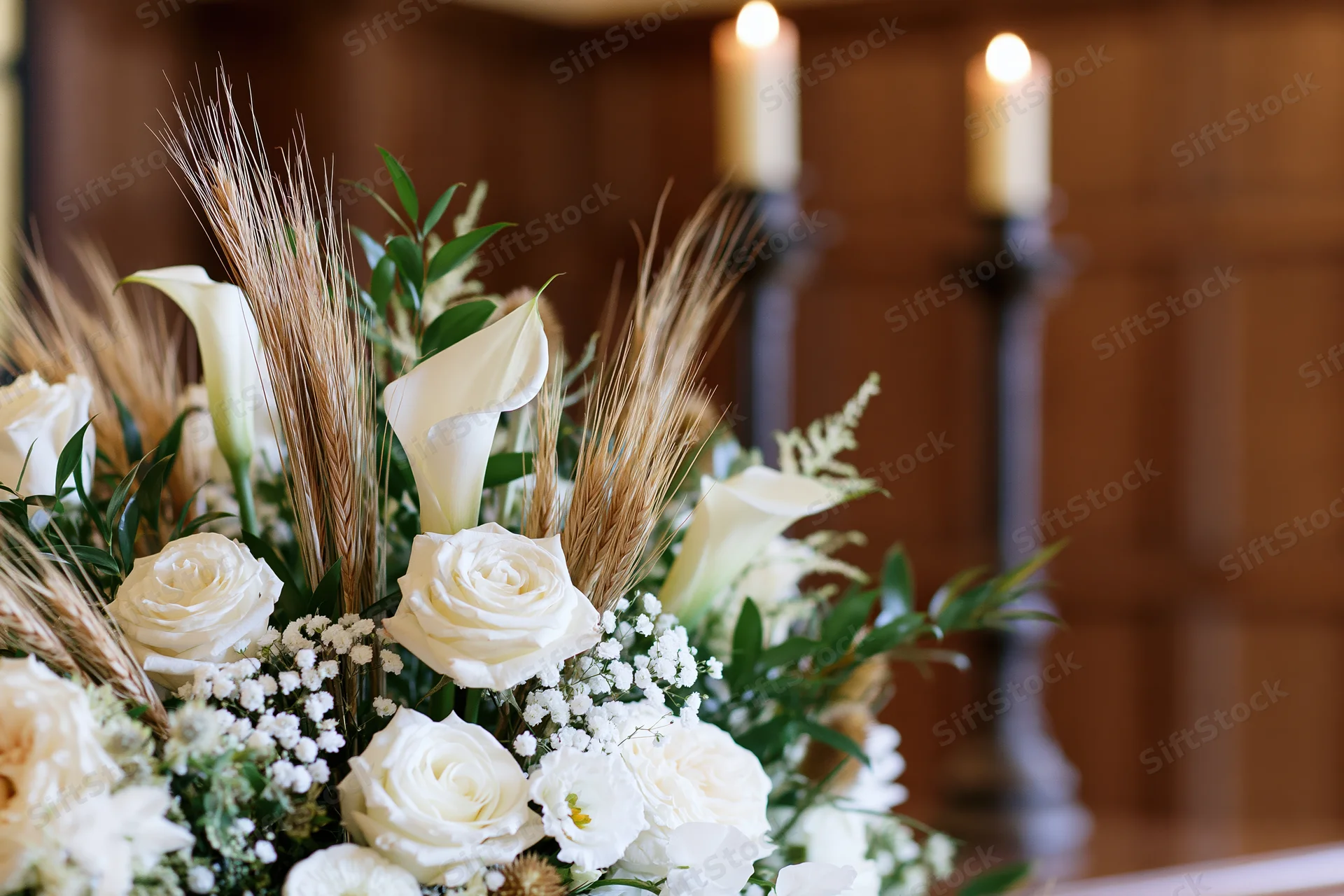 White floral arrangement with roses and calla lilies on an altar with lit candles in a church