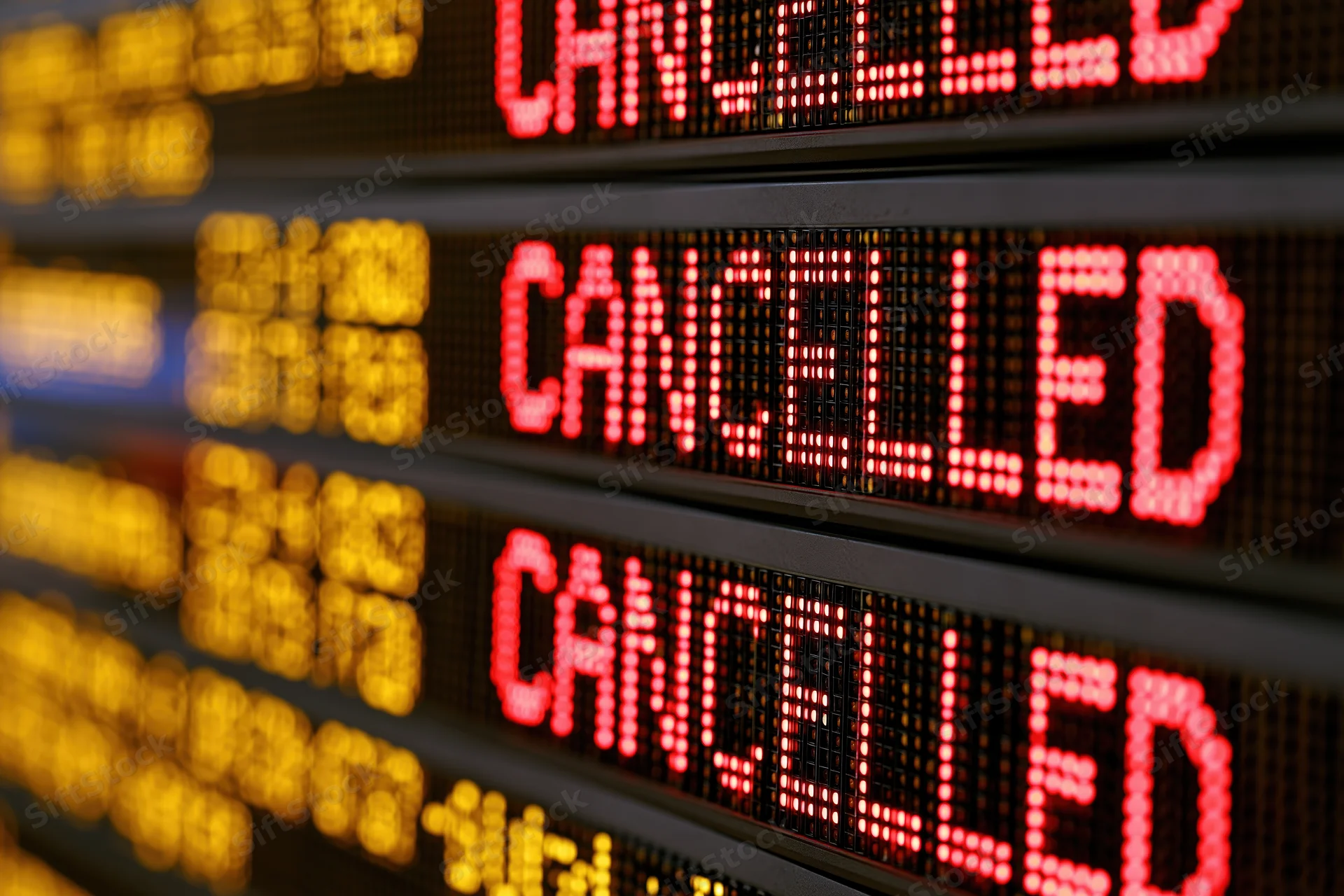 Close-up of airport departure board showing multiple cancelled flights in red led text with blurred yellow flight details in background