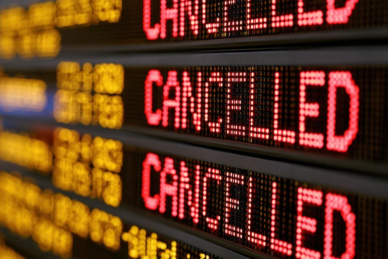 Close-up of airport departure board showing multiple cancelled flights in red led text with blurred yellow flight details in background