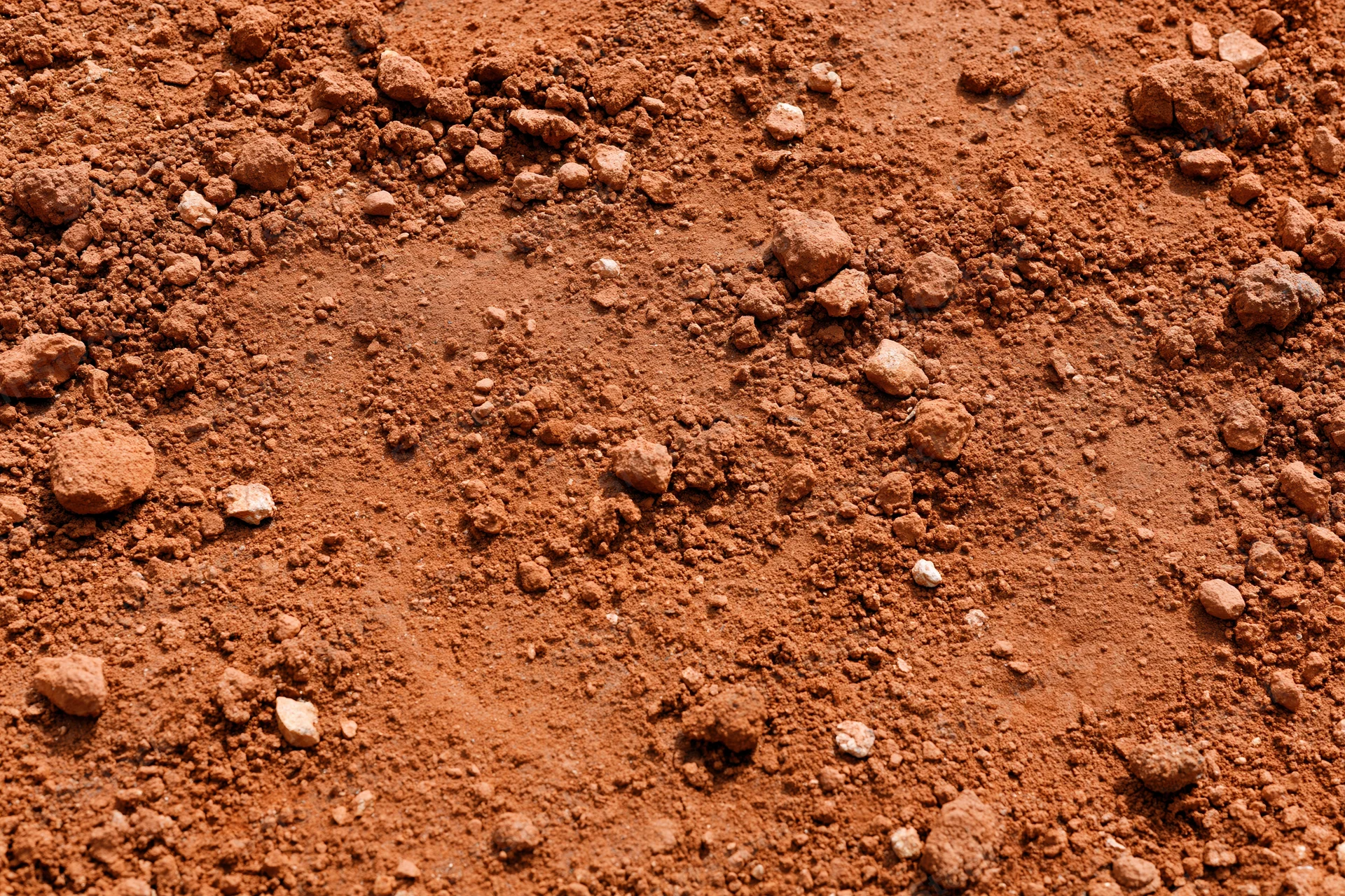 Dry red clay soil surface scattered with small clumps and particles viewed from above