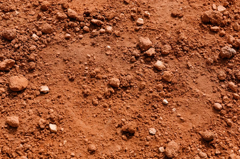 Dry red clay soil surface scattered with small clumps and particles viewed from above