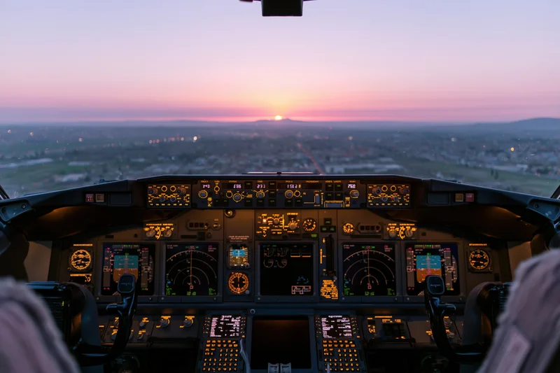 Commercial airliner cockpit interior at sunrise with illuminated instruments and city view ahead