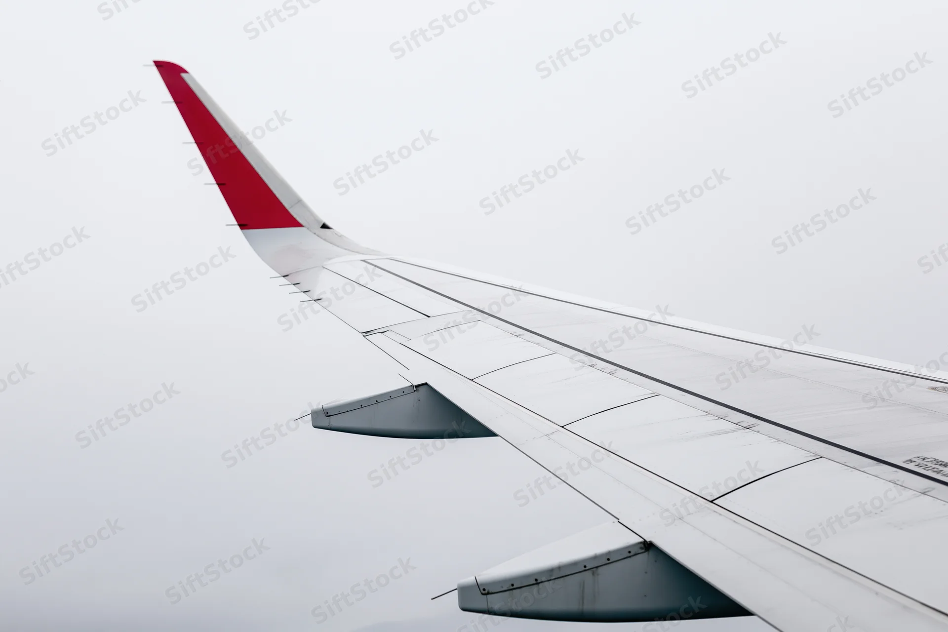 Commercial airplane wing viewed from passenger window during flight in overcast sky