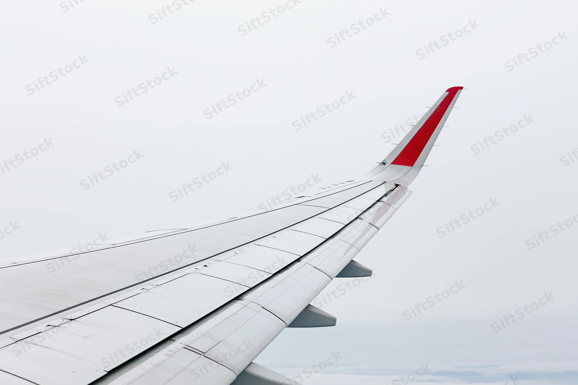 Airplane wing viewed from passenger window during flight above clouds