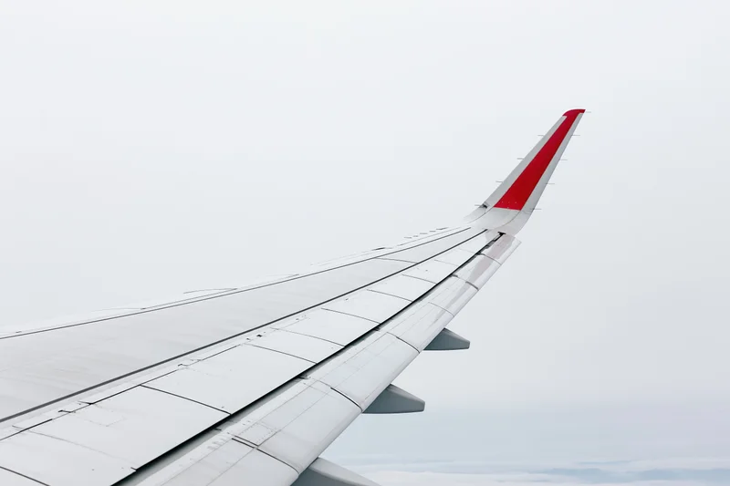 Airplane wing viewed from passenger window during flight above clouds