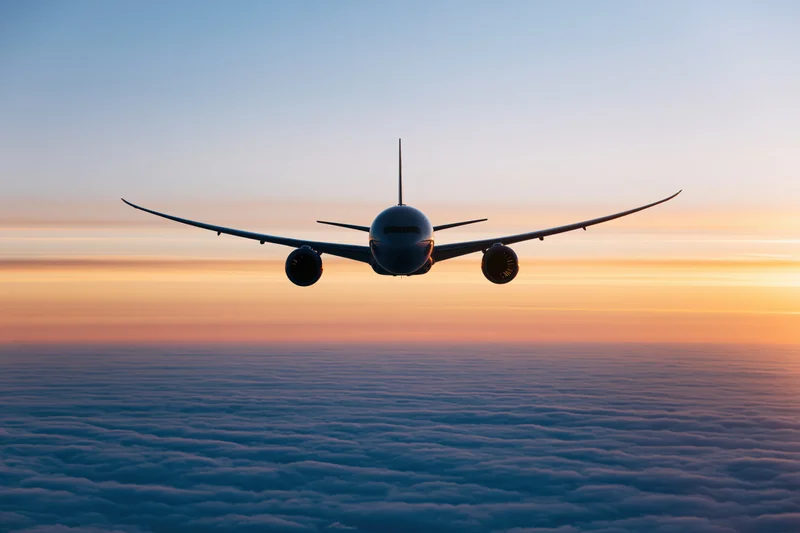 Commercial passenger jet flying above dense cloud layer at sunset