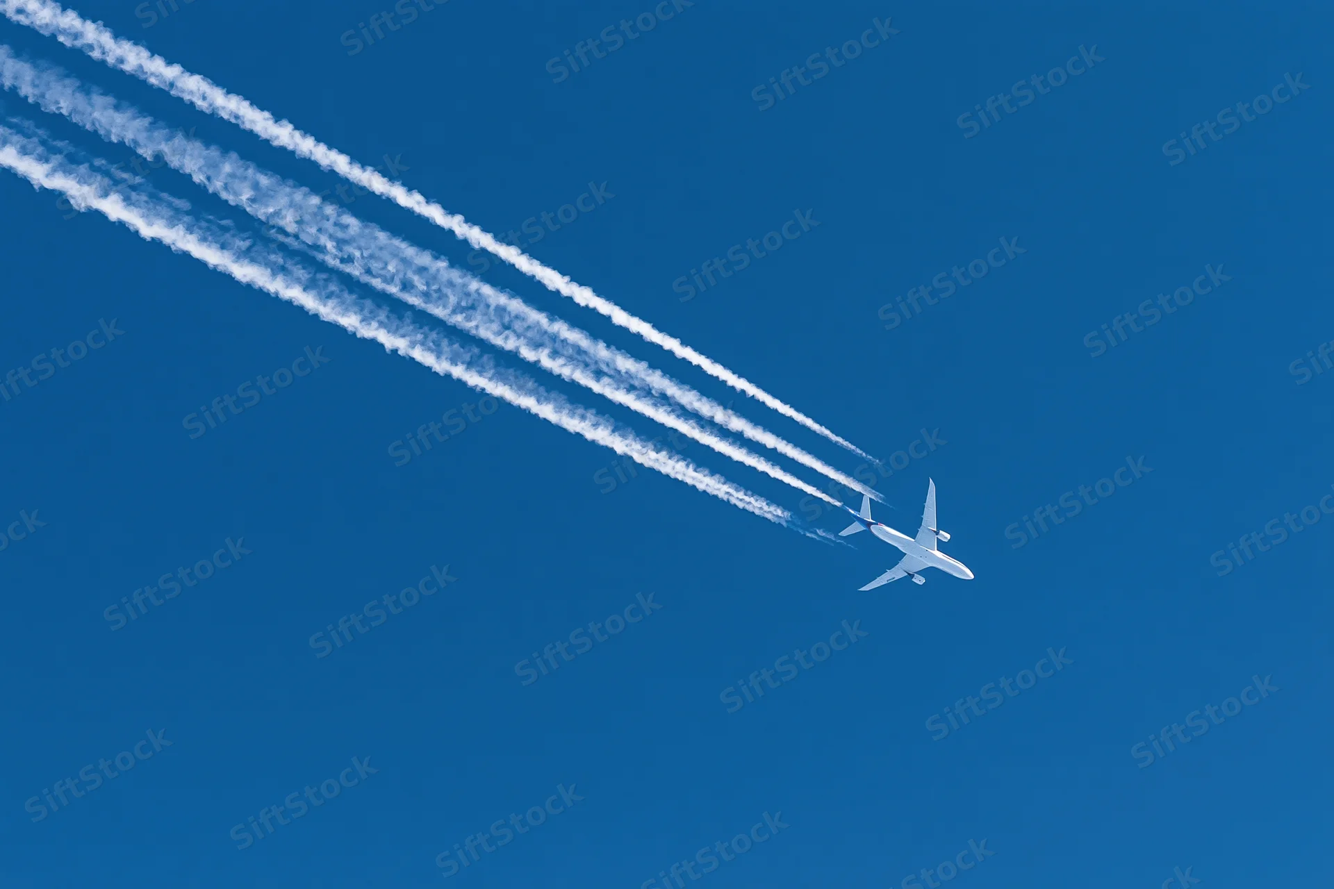 Commercial passenger jet flying at high altitude leaving four contrails in clear blue sky