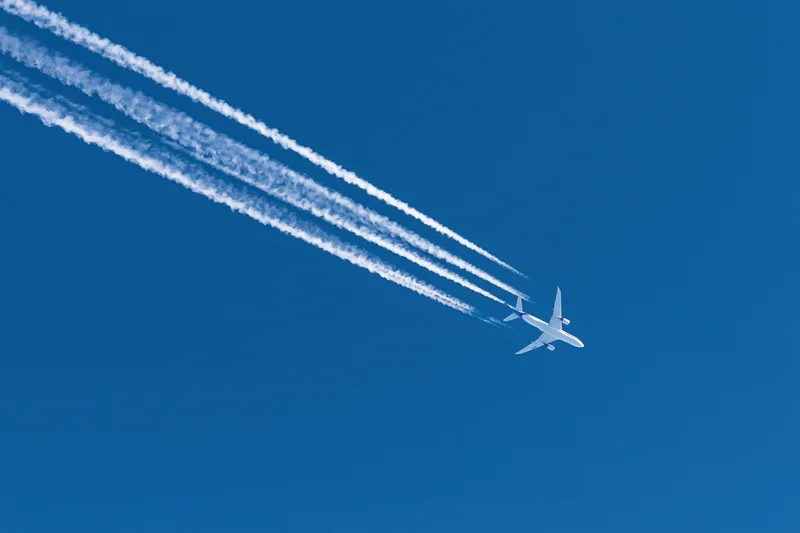 Commercial passenger jet flying at high altitude leaving four contrails in clear blue sky
