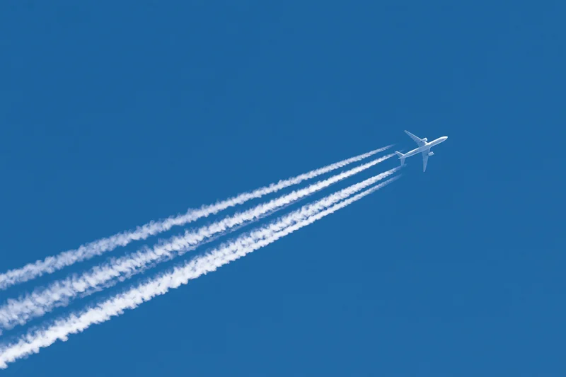 Commercial passenger jet flying at high altitude leaving four contrails in clear blue sky
