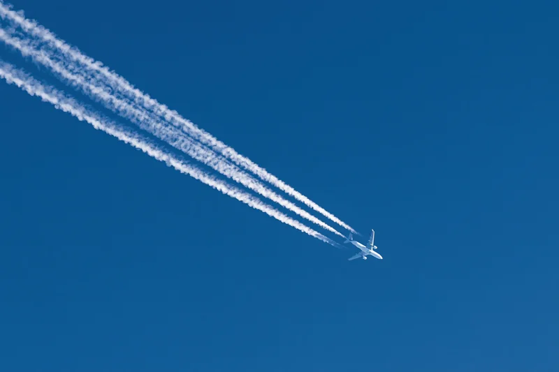 Commercial passenger jet flying at high altitude leaving four contrails in clear blue sky