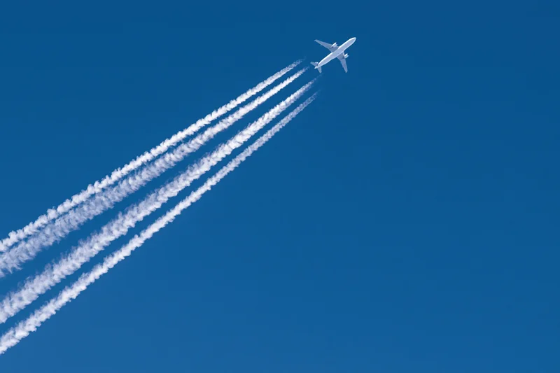 Commercial passenger jet flying at high altitude leaving four contrails against clear blue sky