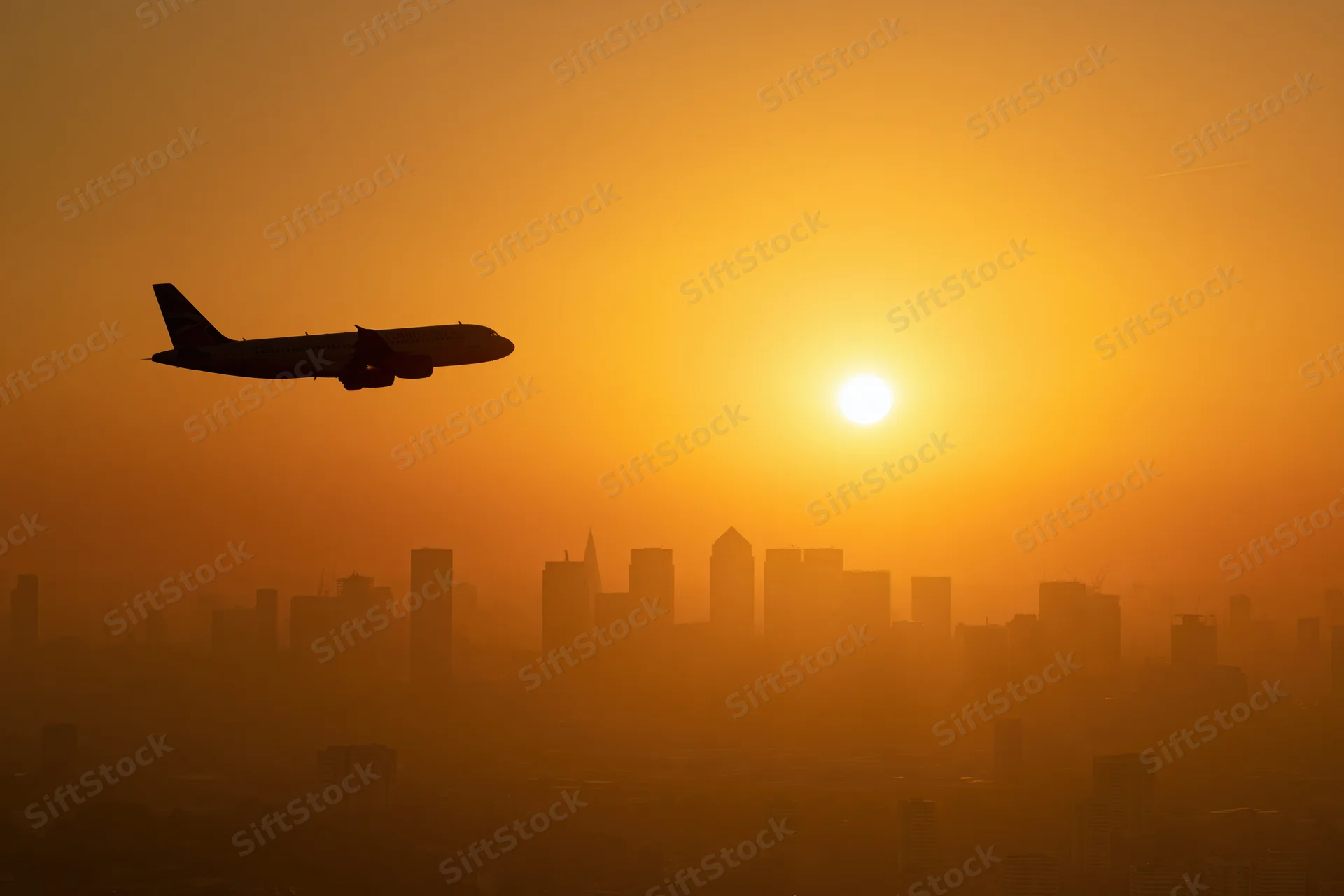 Commercial passenger jet silhouetted against glowing sunset over city skyline