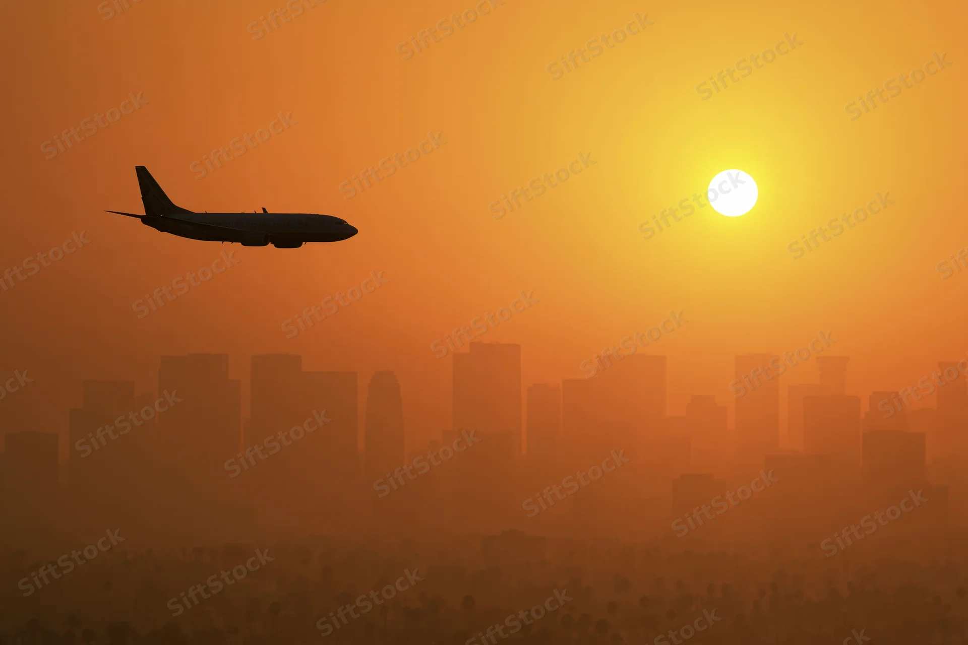 Commercial passenger jet silhouetted against glowing sunset over city skyline