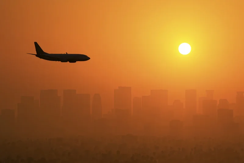 Commercial passenger jet silhouetted against glowing sunset over city skyline